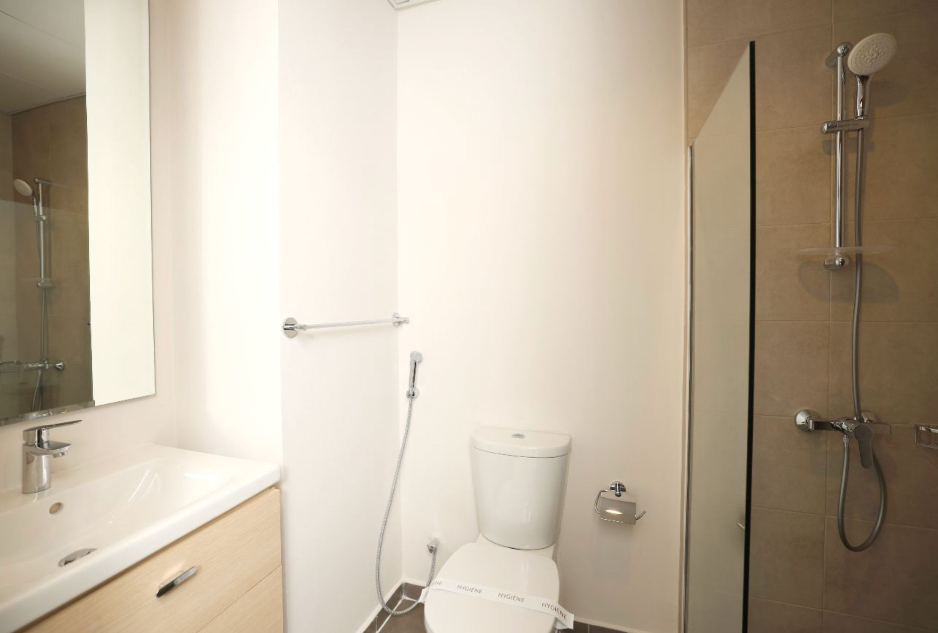 Bathroom with a white toilet, shower, sink, and mirror. Beige walls and cabinet.