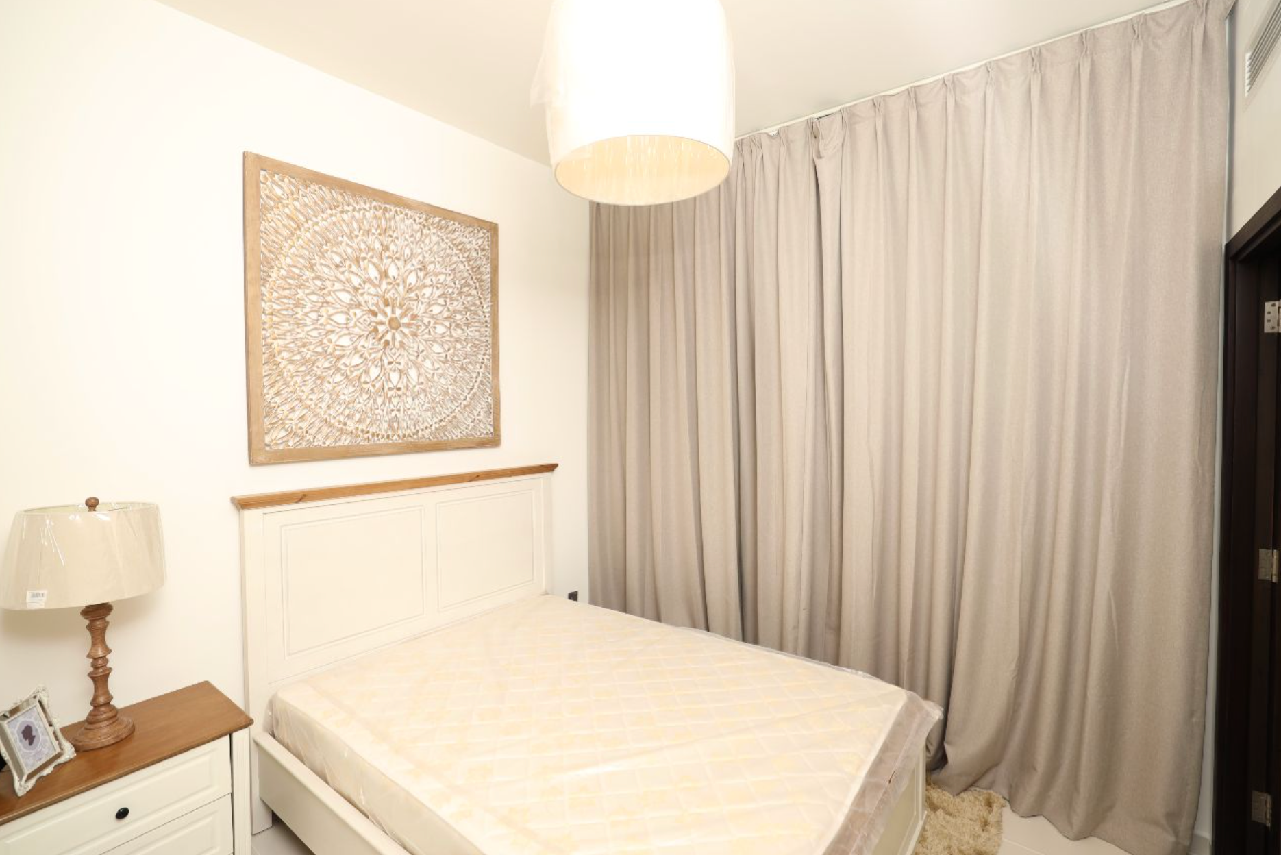 Bedroom with white bed, beige curtains, lamp, and decorative wall art.