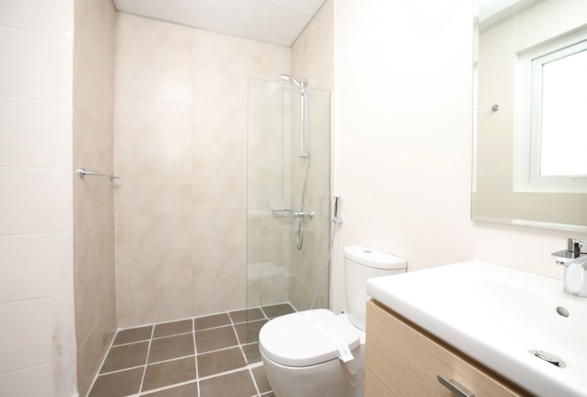Bathroom with a shower, toilet, and sink. Beige and gray color scheme, modern design.