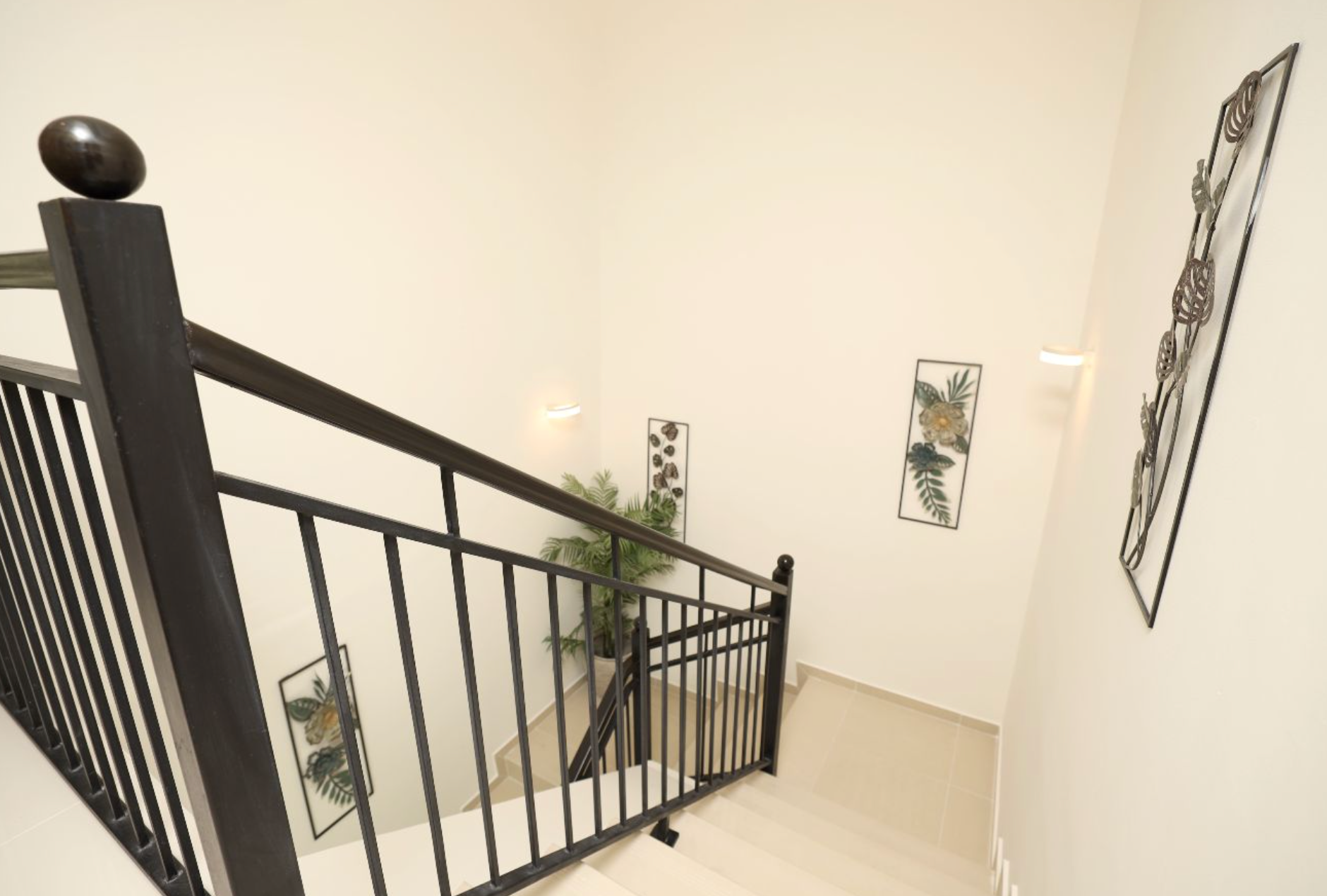 View from top of stairs with black railing and neutral walls, decorated with art and greenery.