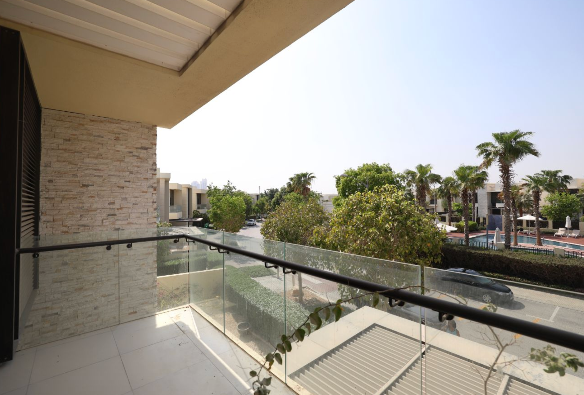 Balcony view of street with palm trees and modern buildings on a sunny day.