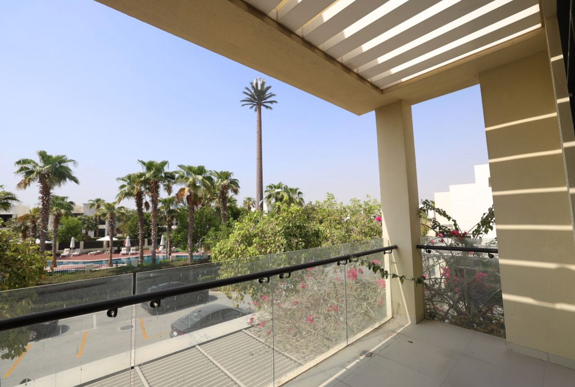 Balcony view of palm trees, a tall structure, and a clear blue sky.