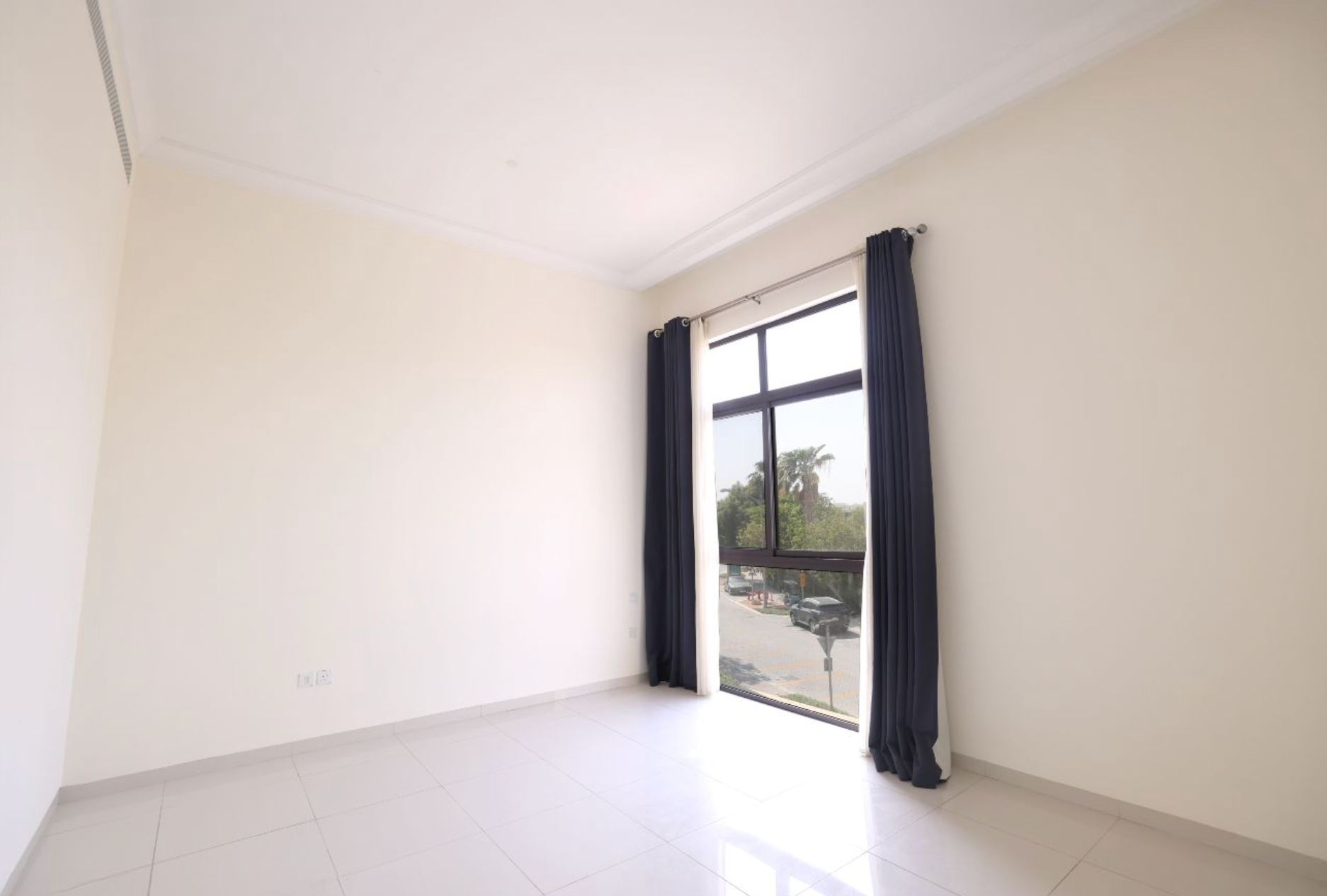 Empty room with beige walls, tiled floor, and a window with dark curtains.