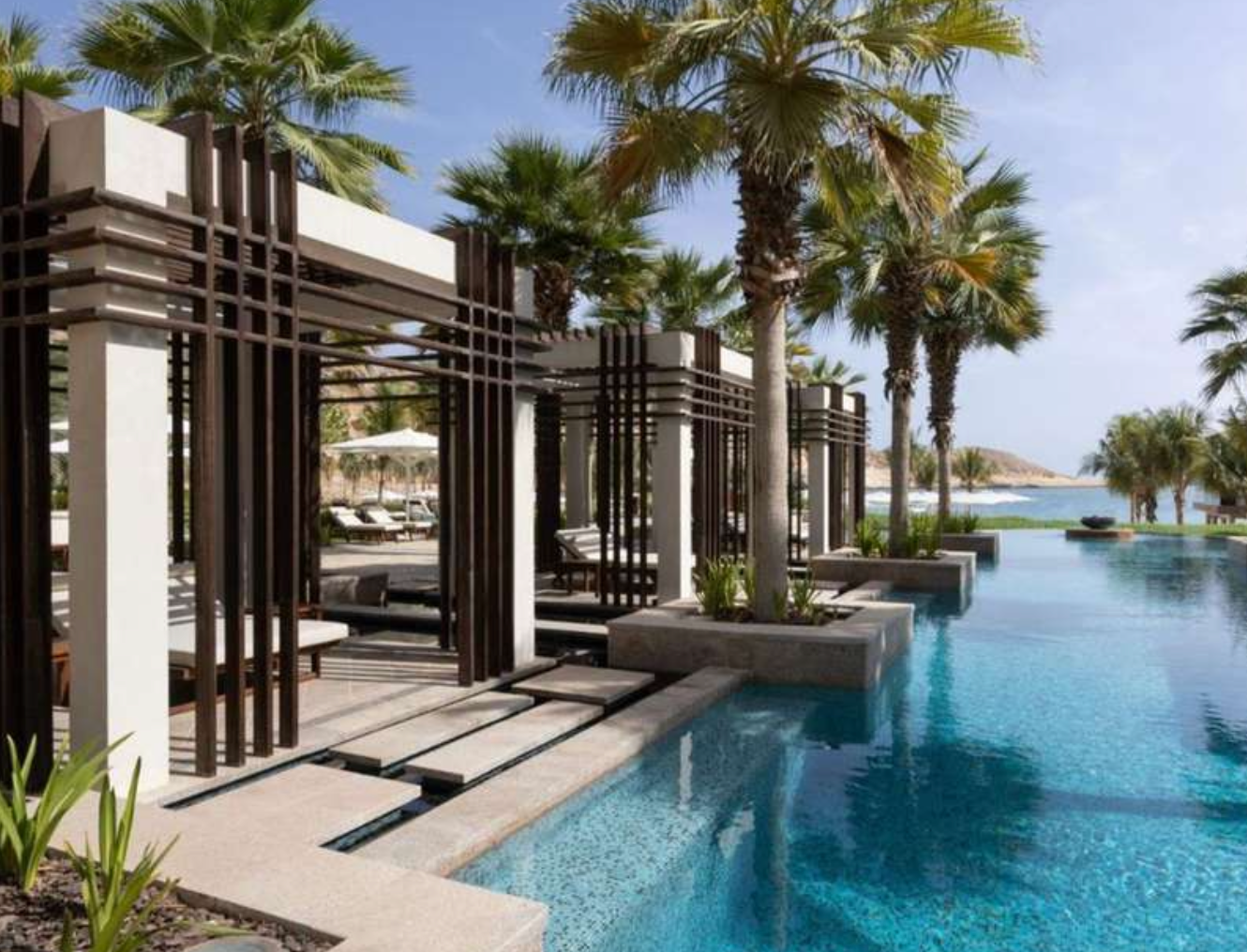 Luxurious resort pool with cabanas, palm trees, and ocean view.