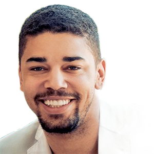 Man smiling, close-up. He has short dark hair and a beard, wearing a light-colored jacket.