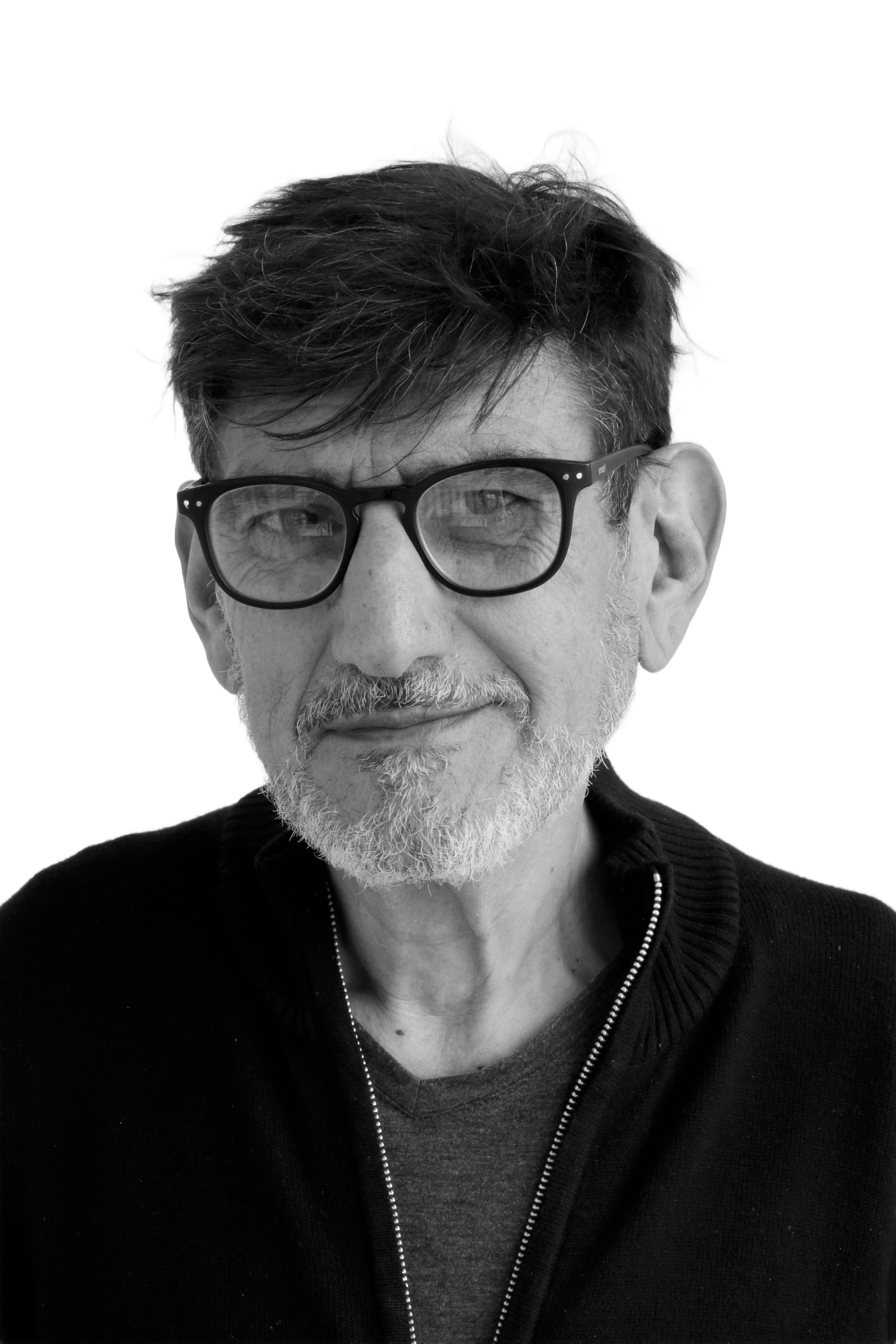 Man with glasses and beard smiles, wearing a dark sweater against a white backdrop.