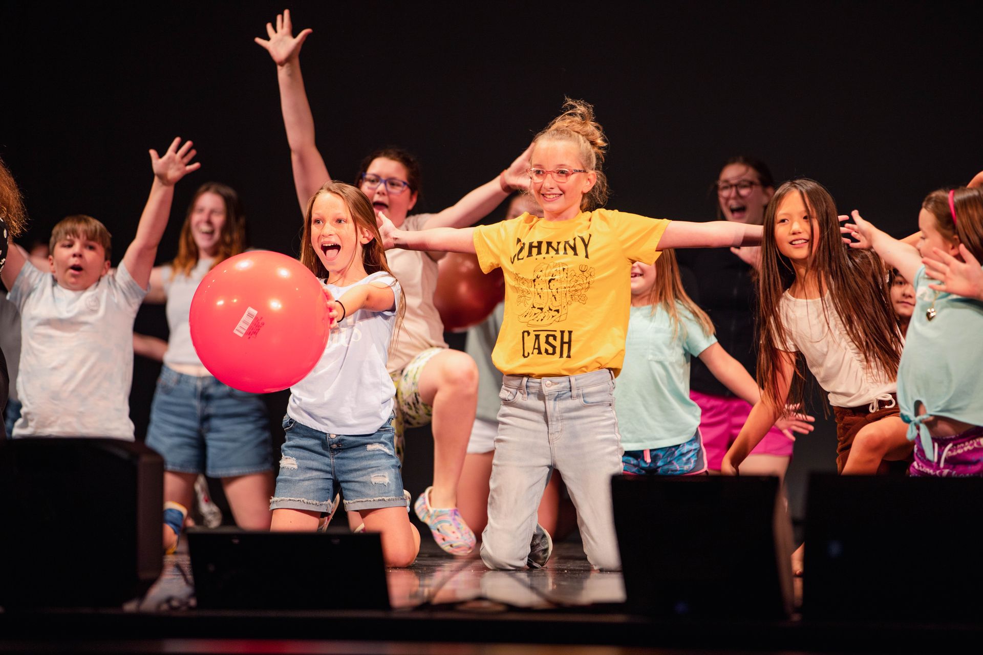 A group of children at Summer Theater Camp are standing on a stage holding balloons.