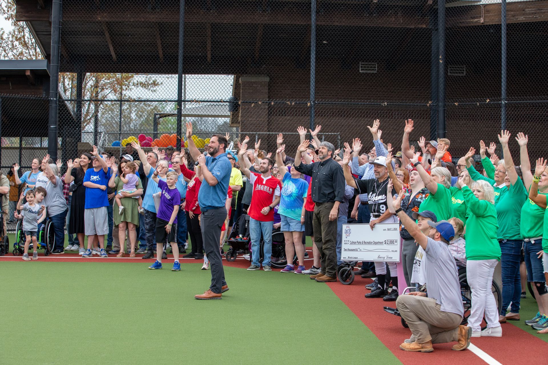 A group of people are standing on a baseball field with their hands in the air.