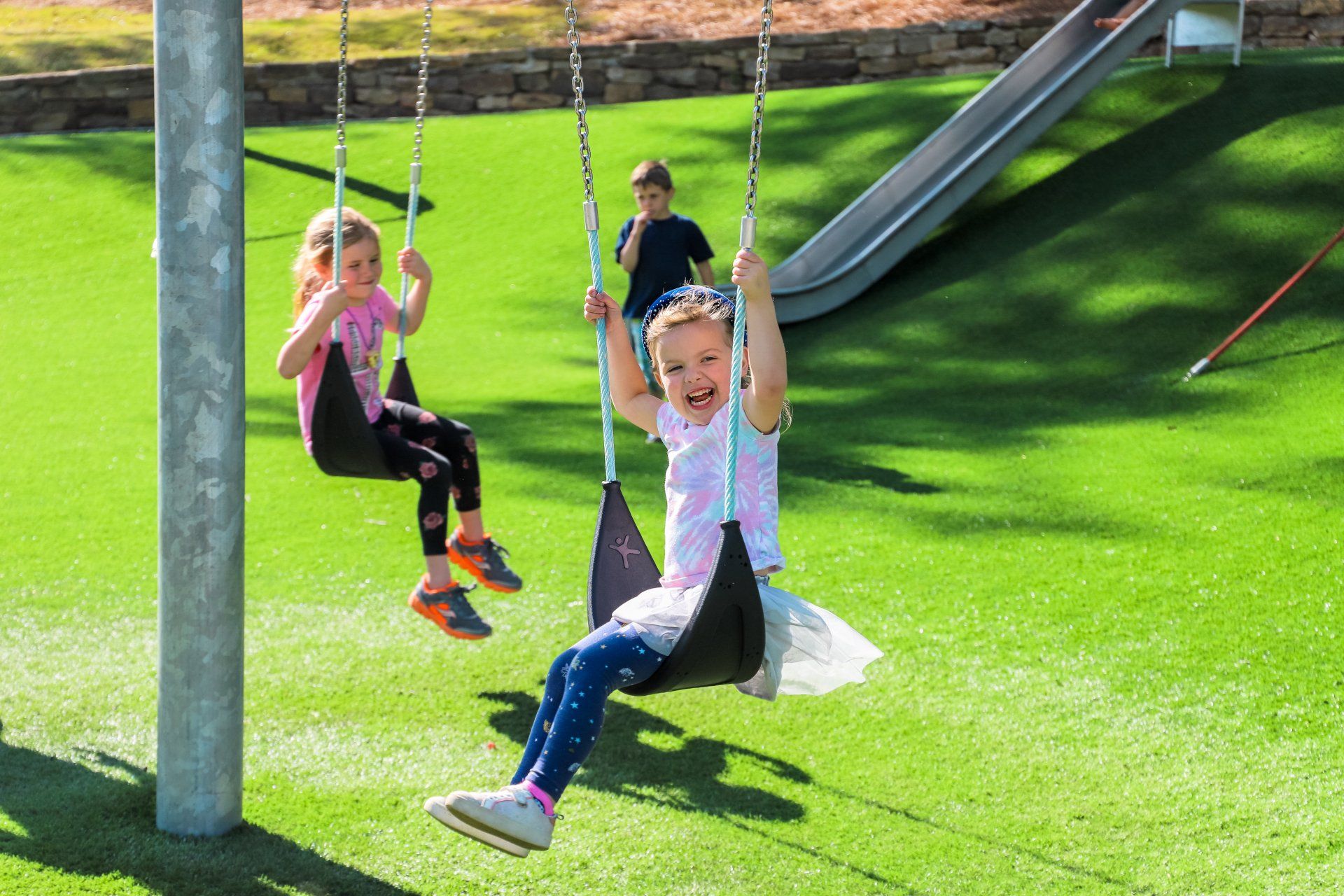 Two little girls are sitting on swings at a playground.