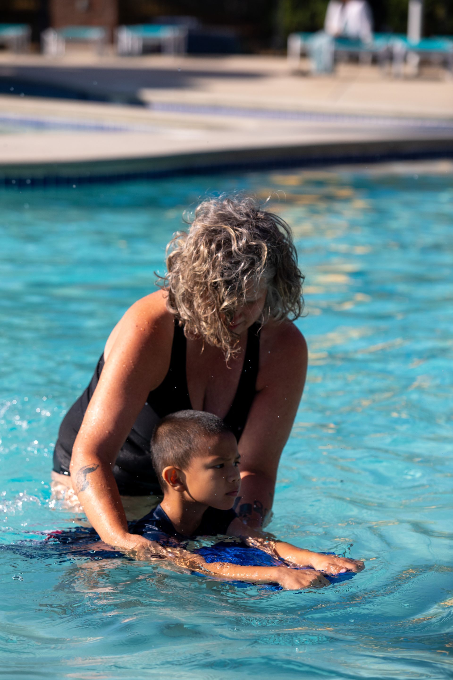 A woman is teaching a young boy how to swim in a swimming pool.