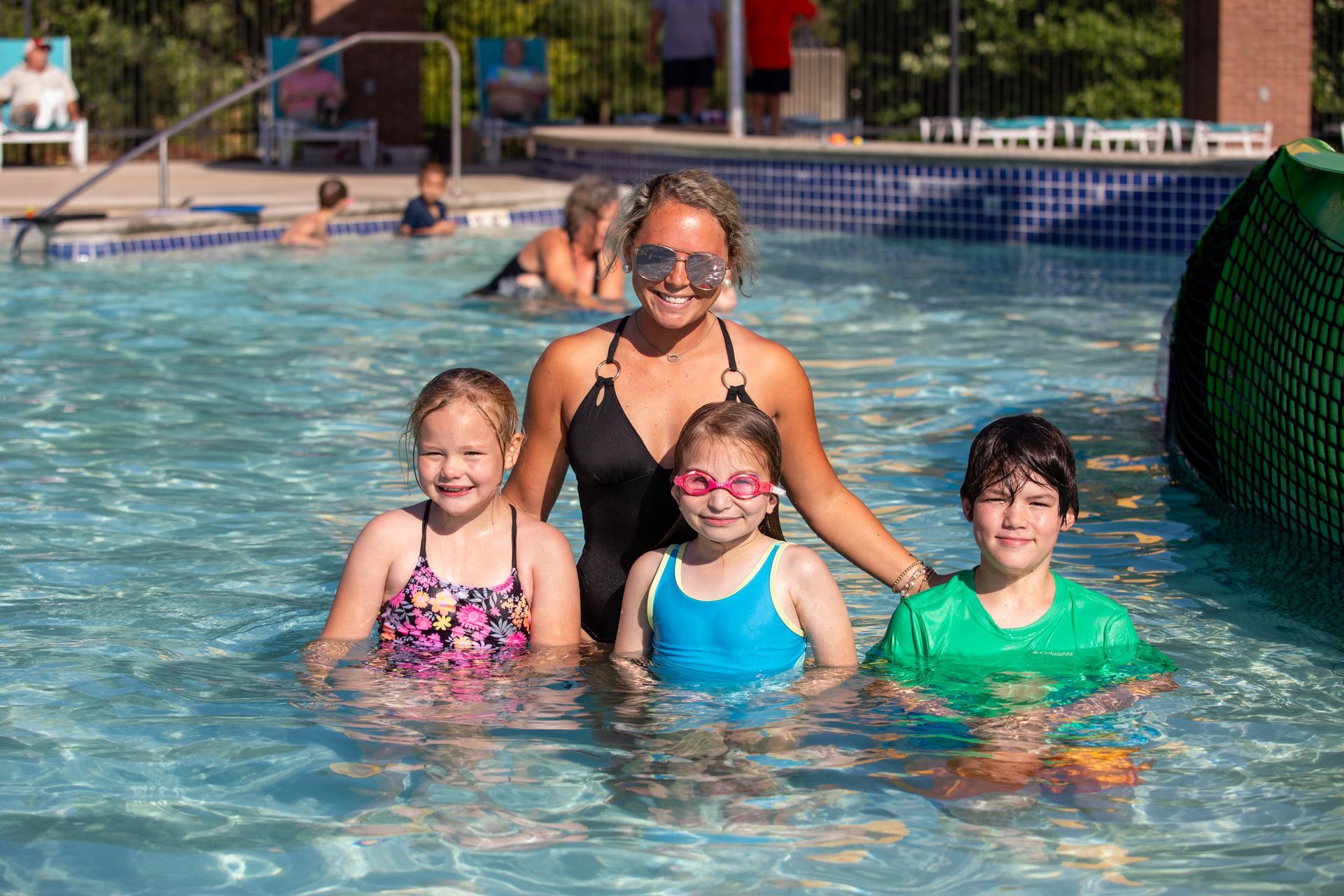 A swim instructor and three children pose for a picture in a swimming pool.