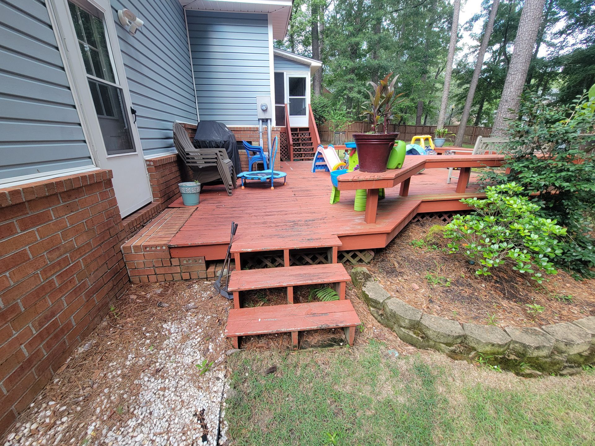 A wooden deck with stairs leading up to it is in the backyard of a house.