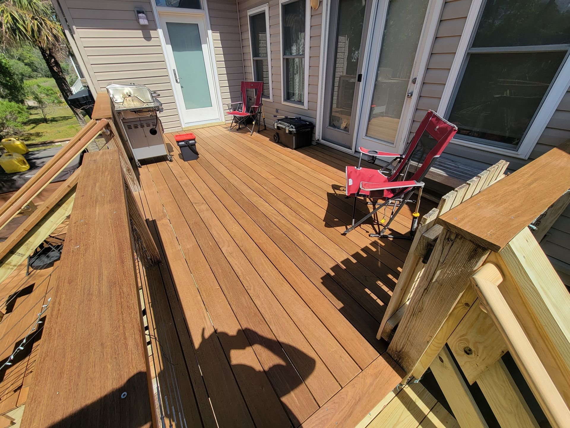 A wooden deck with chairs and a grill on it in front of a house.