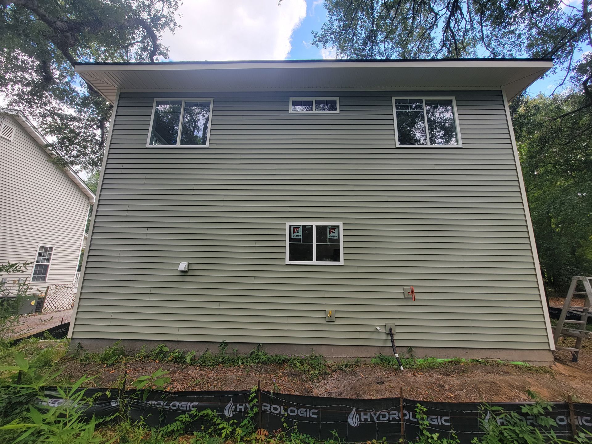 The back of a house with a green siding and white windows.