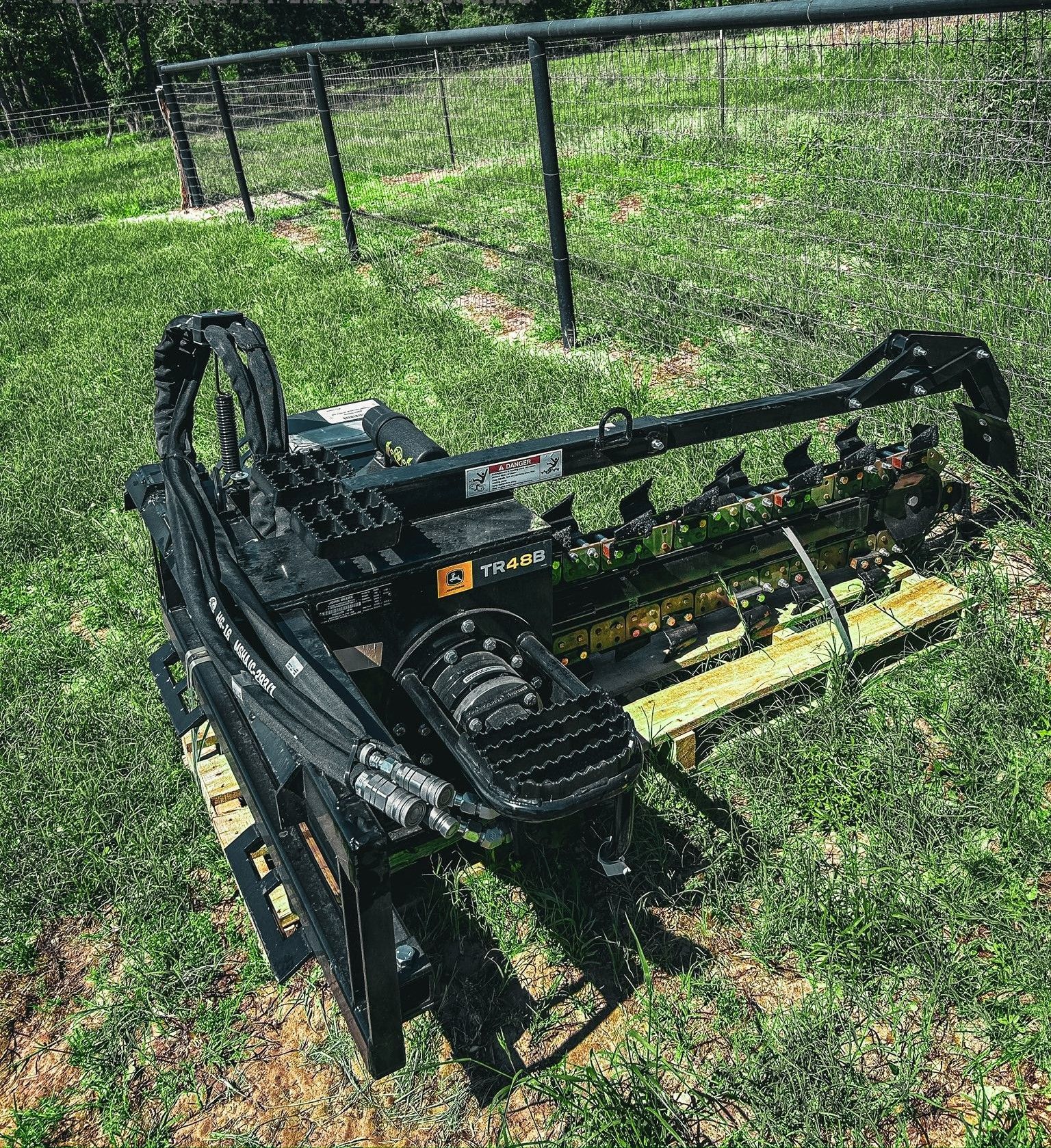 A black trencher on a wooden pallet, on green grass, in front of a fence.