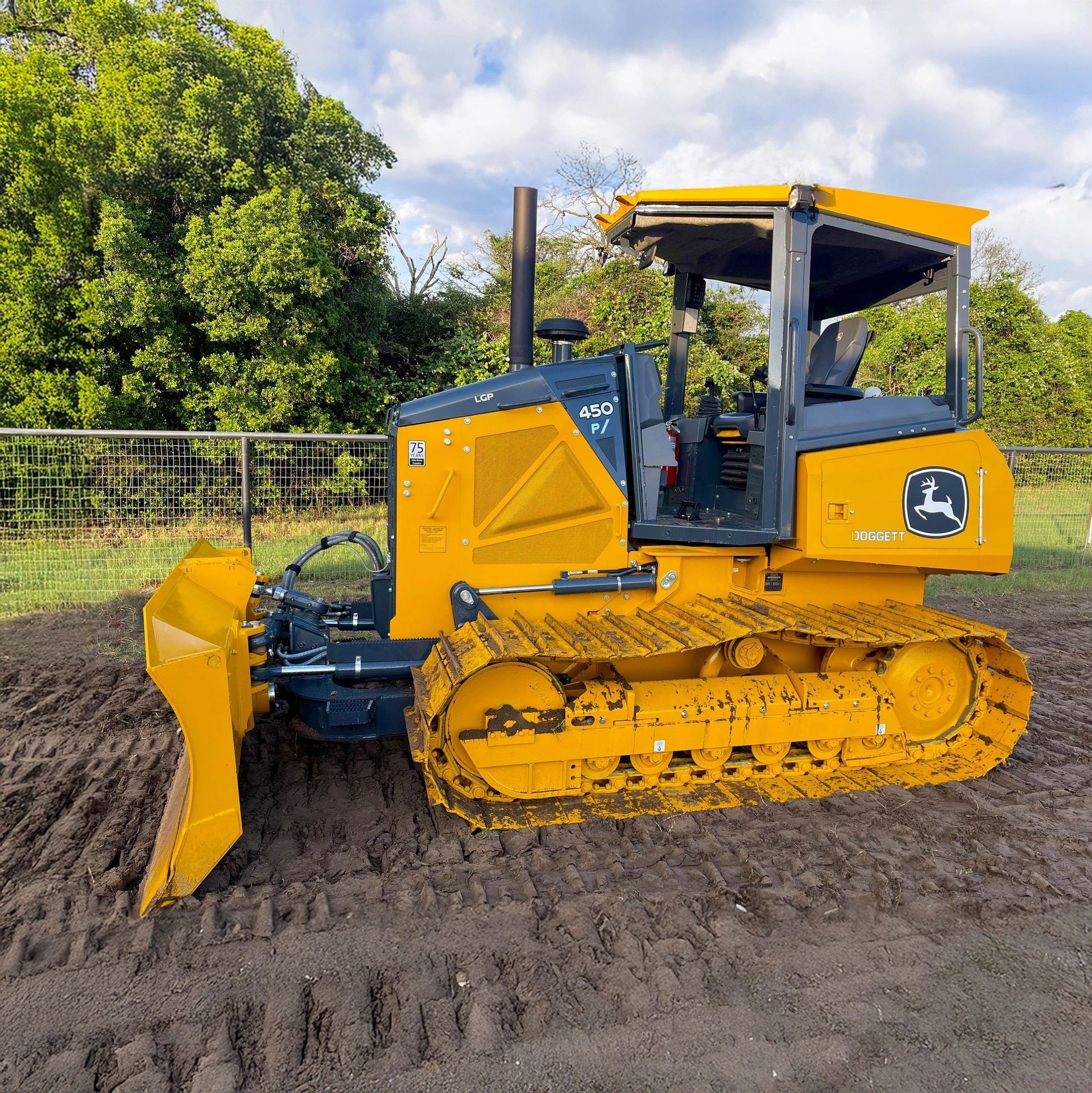 Yellow John Deere bulldozer parked on a dirt surface. It has a black cab, tracks, and a front blade.