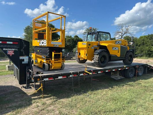 A yellow scissor lift and a yellow telehandler on a flatbed trailer, ready for transport.  The setting is outdoors on a sunny day.