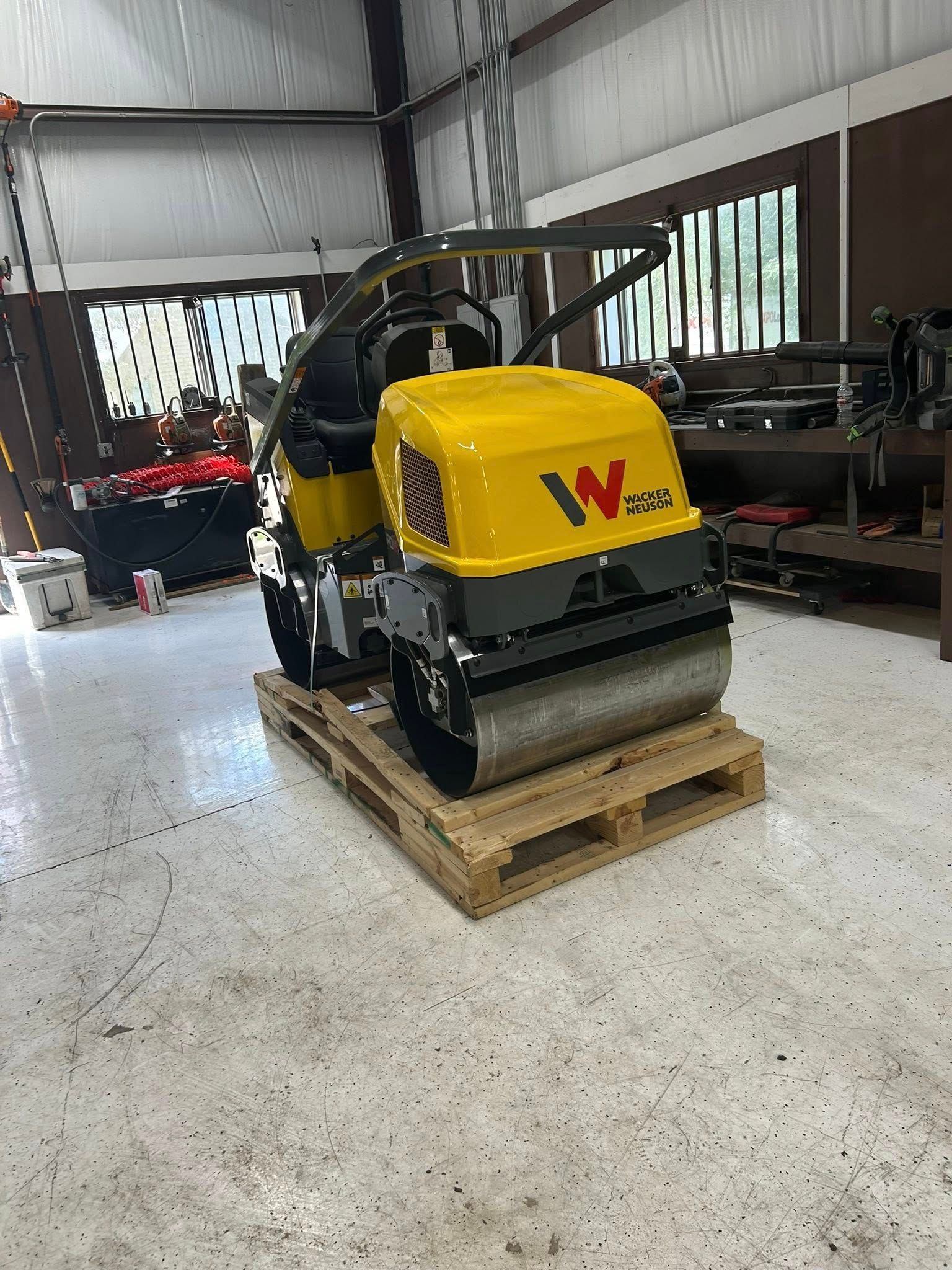A small, yellow and black construction roller on a wooden pallet inside a workshop.