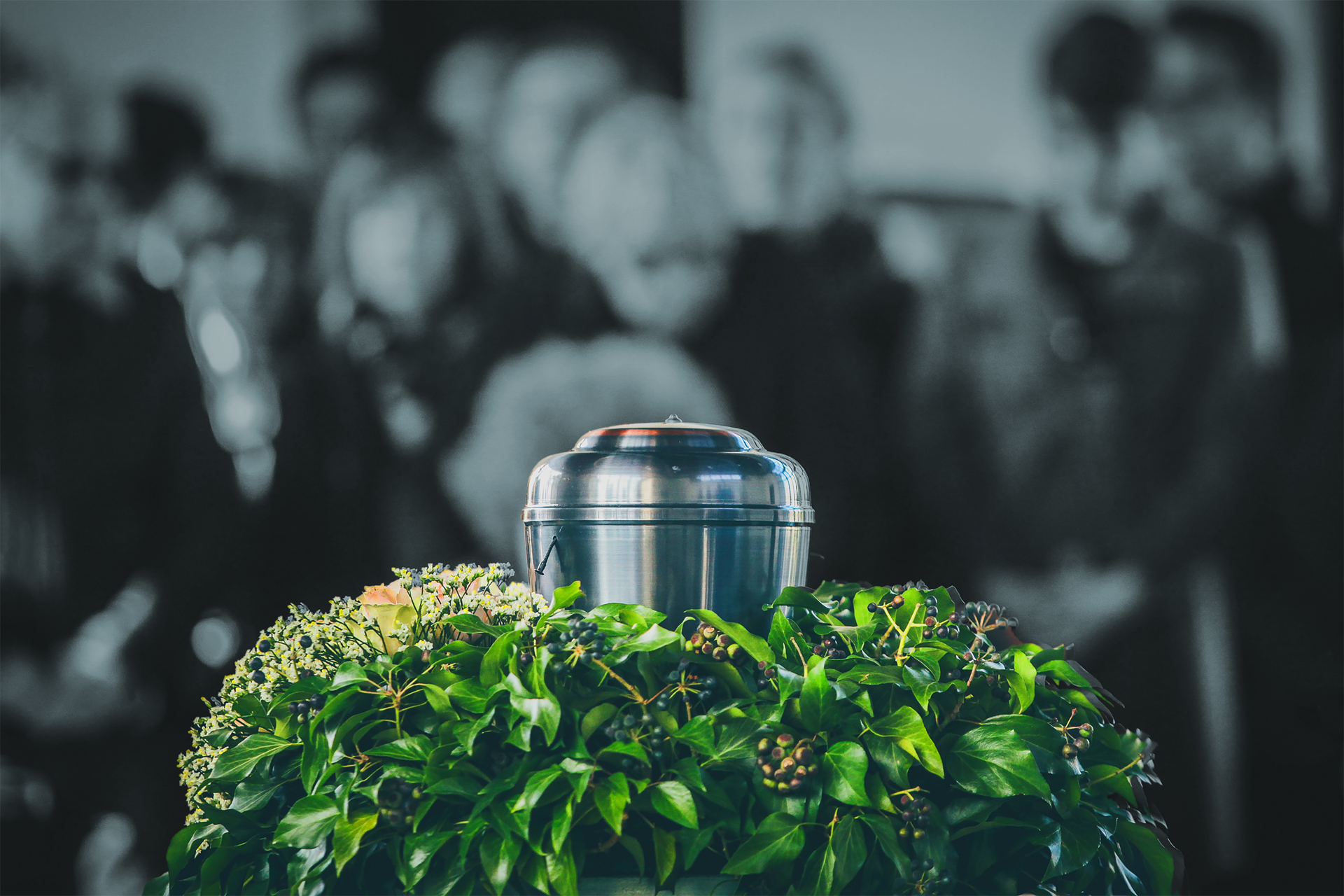 a black urn with silver leaves sits on a table next to a red rose