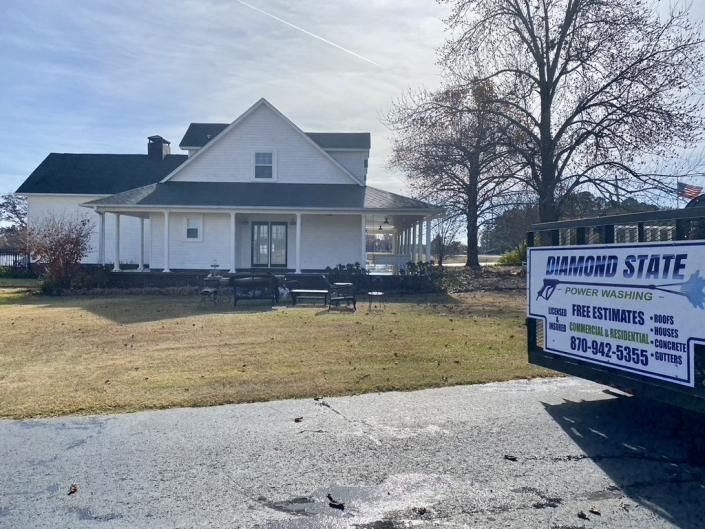 White house with porch in a yard; a truck on the right has a “Diamond State” sign.