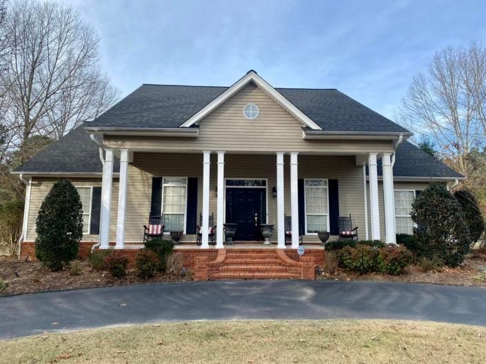 Front porch of a tan house with white columns, black roof, and brick steps under a blue sky