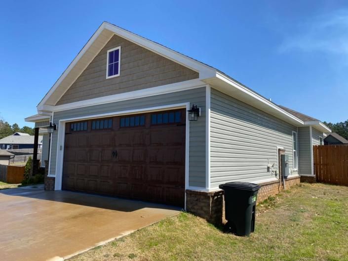 Suburban house exterior with brown garage door, beige siding, and a driveway under a blue sky