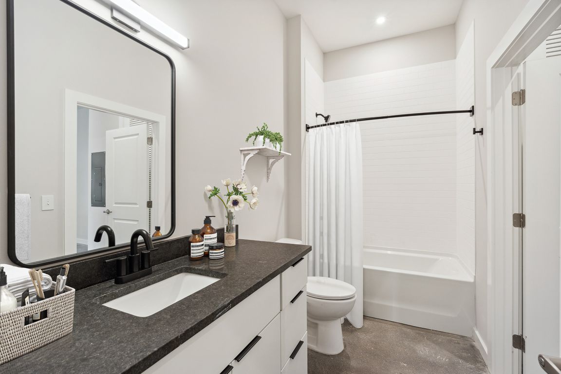 Modern bathroom with a large mirror, dark countertop, and white fixtures.