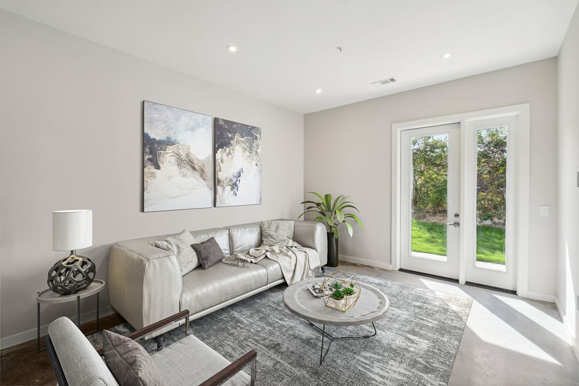 Living room with beige couch, gray rug, artwork, and French doors leading to a yard.