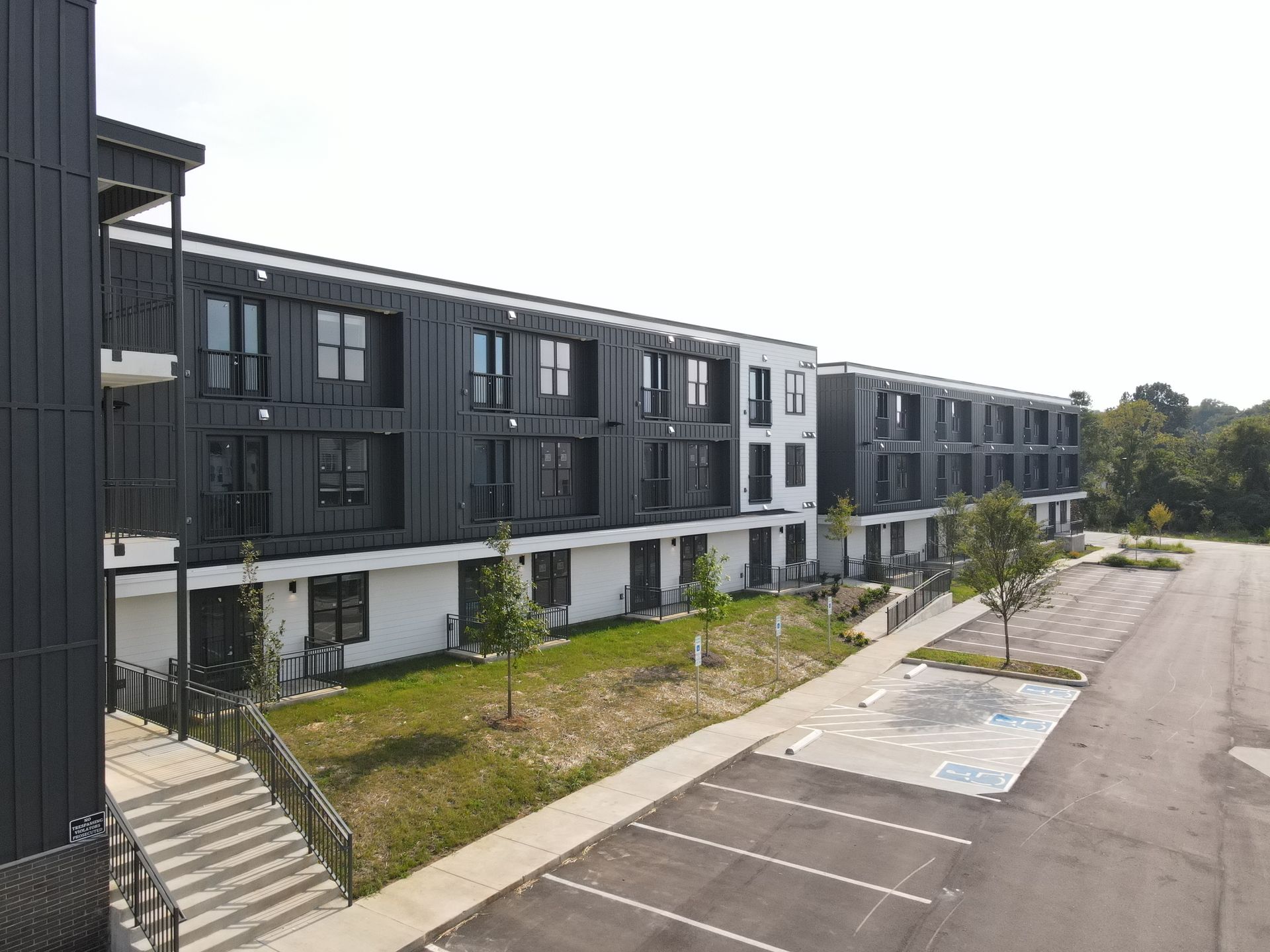 Modern black and white apartment building with parking area.