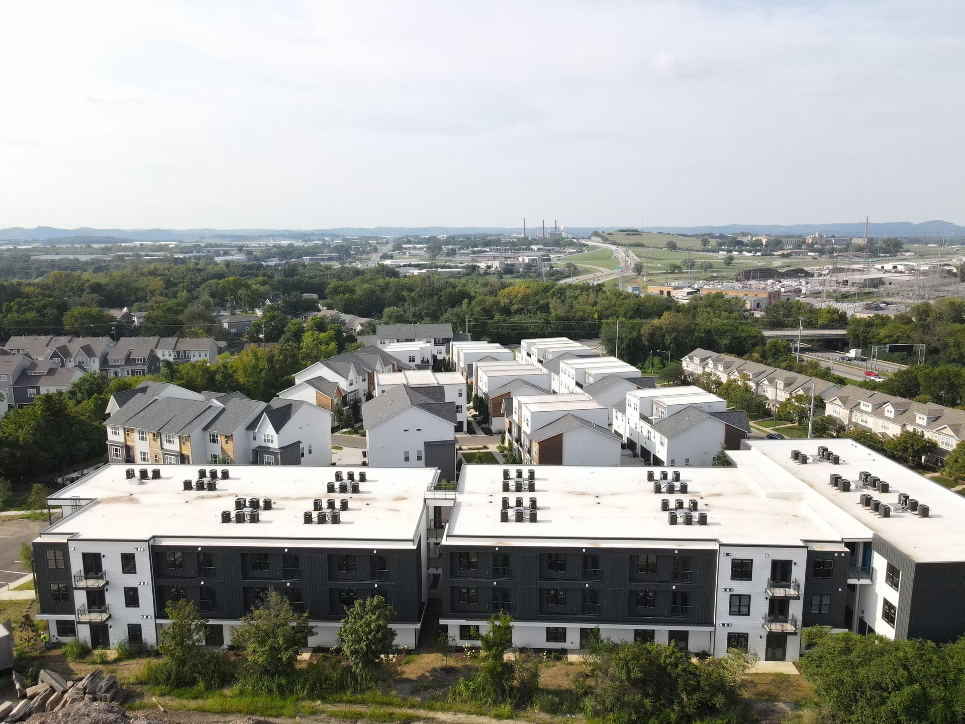 Aerial view of modern apartment buildings with white and dark gray exteriors, surrounded by trees.