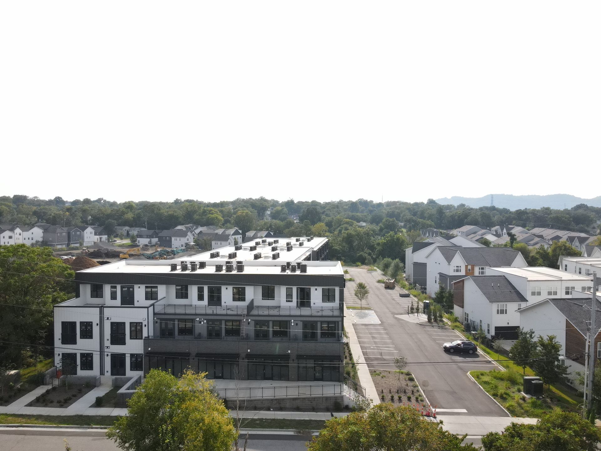 Multi-story modern townhouses with a flat roof, near a street lined with trees and other houses.