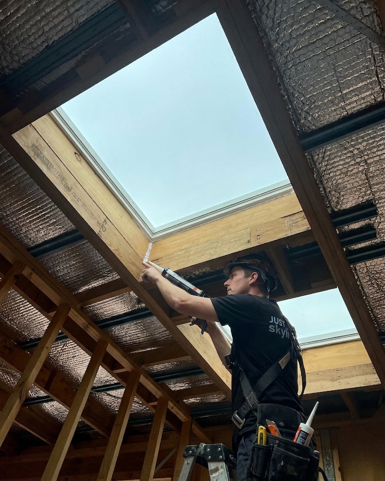 Worker installing a skylight panel in a wooden roof frame
