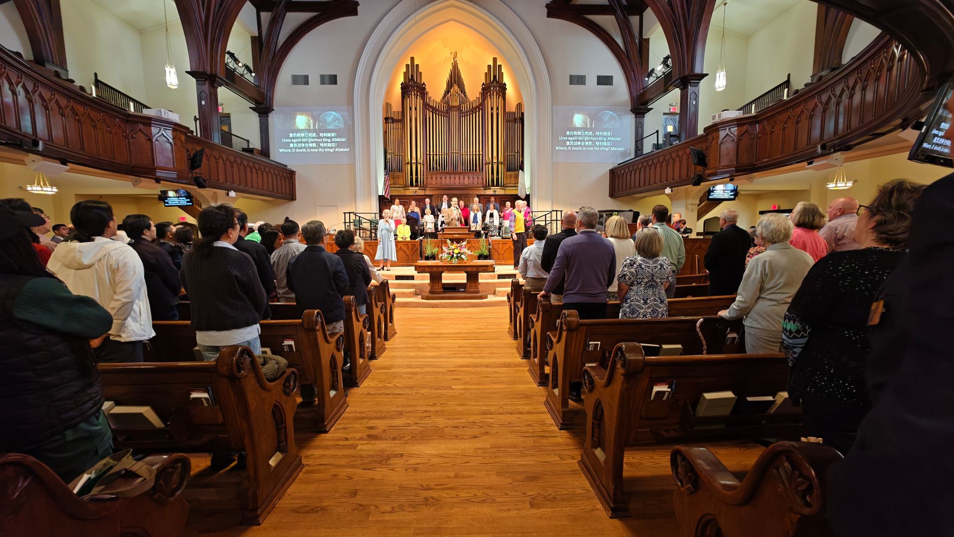 从圣所向中殿过道尽头望去。人们面向前方正在歌唱，唱诗班则立于管风琴之前。