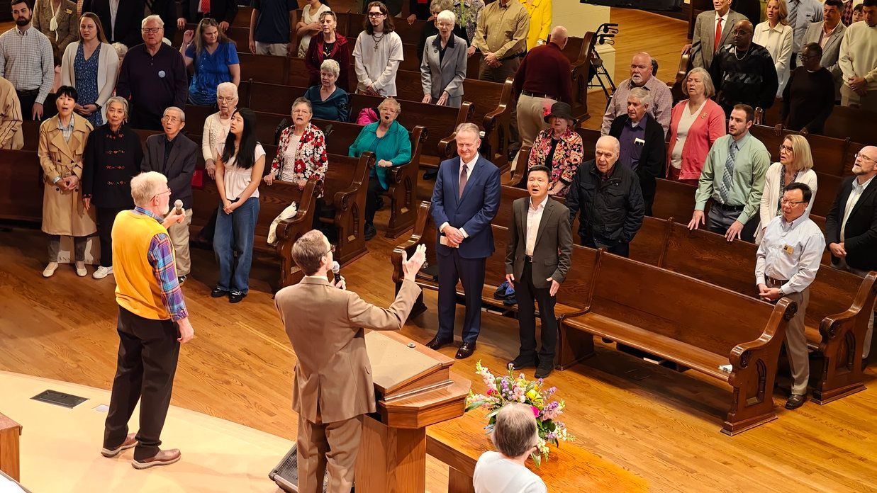 The congregation sings together, shown  looking out at the pews. The pastors are in the front row and singers in the front. 