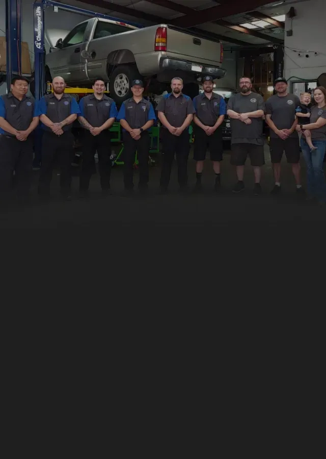 Row of staff in front of truck on lift in our garage | Tedious Auto Repair