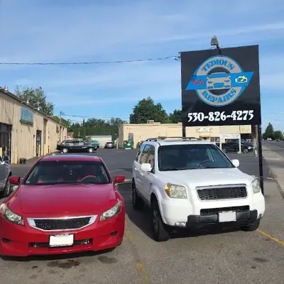 Red car and white SUV parked by sign outside our shop | Tedious Auto Repair