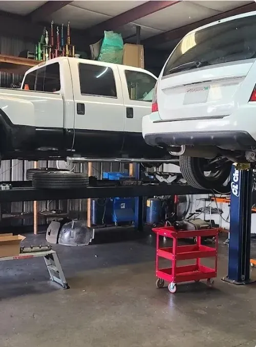 White truck and white SUV raised on lifts in garage | Tedious Auto Repair