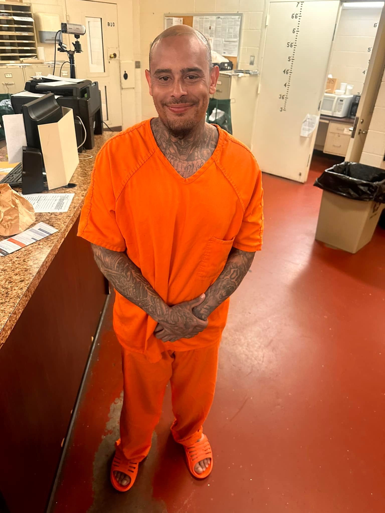 A man in an orange jumpsuit is standing in a room with his arms crossed.