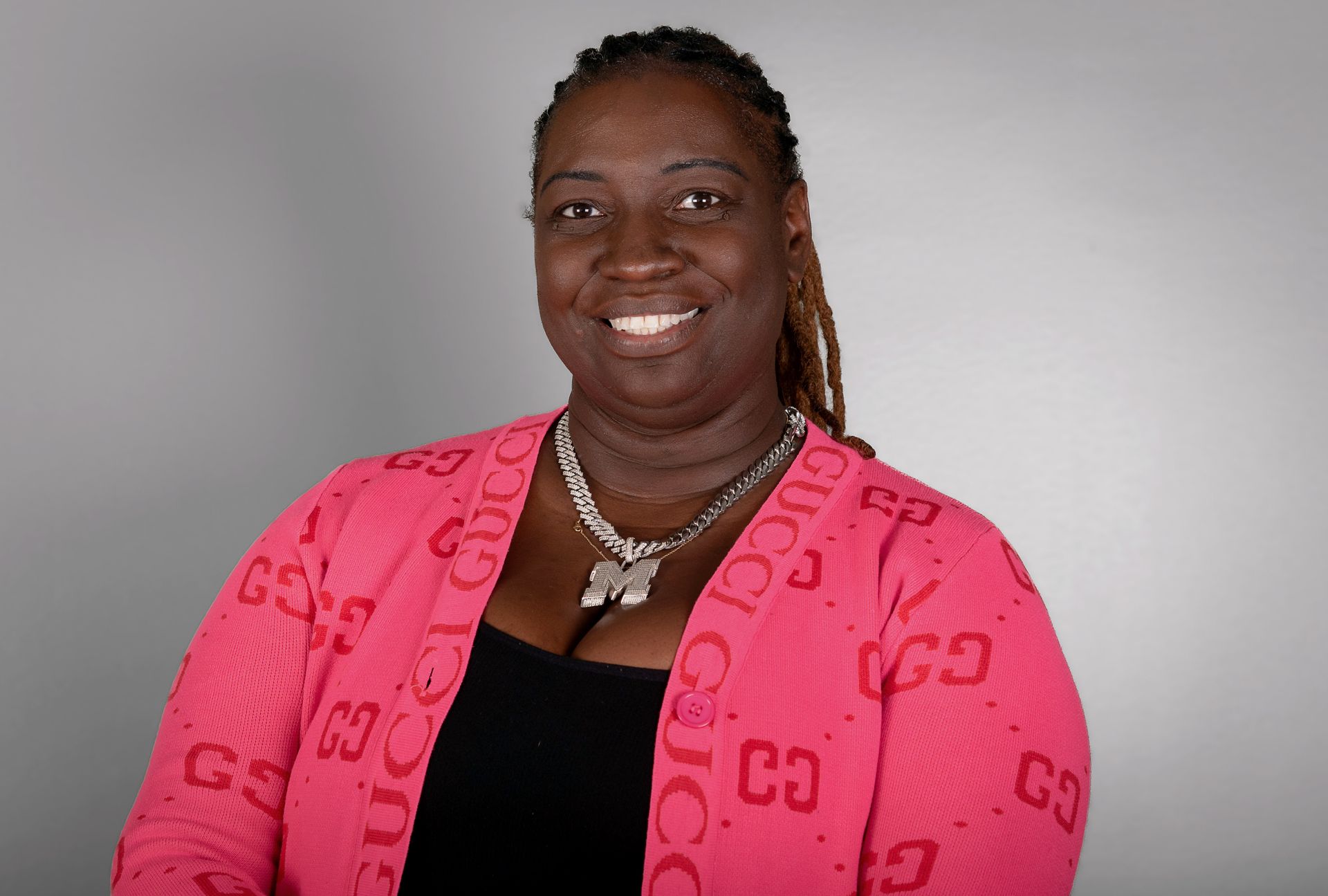 Woman in a pink Gucci cardigan smiles at the camera. Gray backdrop.