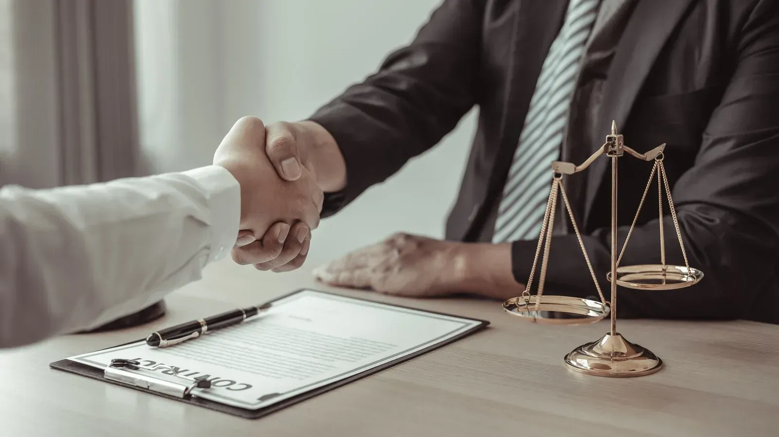 A lawyer is shaking hands with a client in front of a scale of justice.