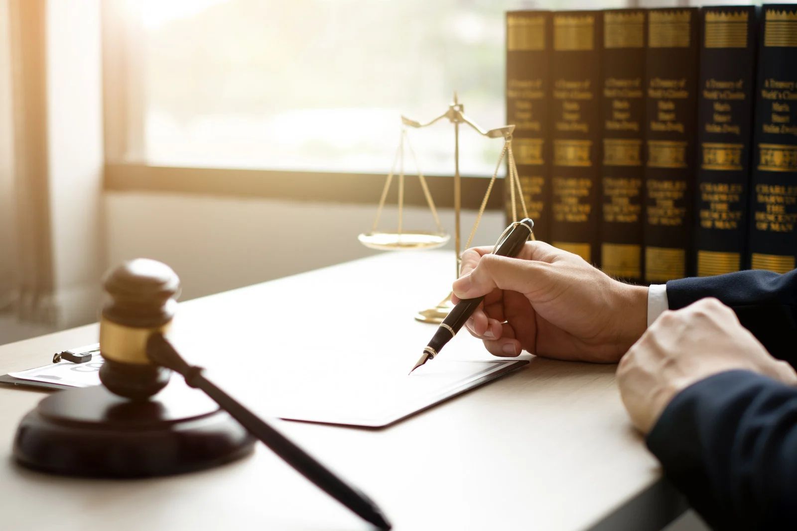 Lawyer writing on paper, scales of justice, gavel, law books in background.