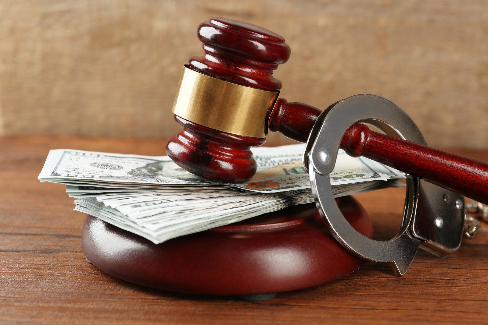 A judge 's gavel and handcuffs on top of a pile of money on a wooden table.