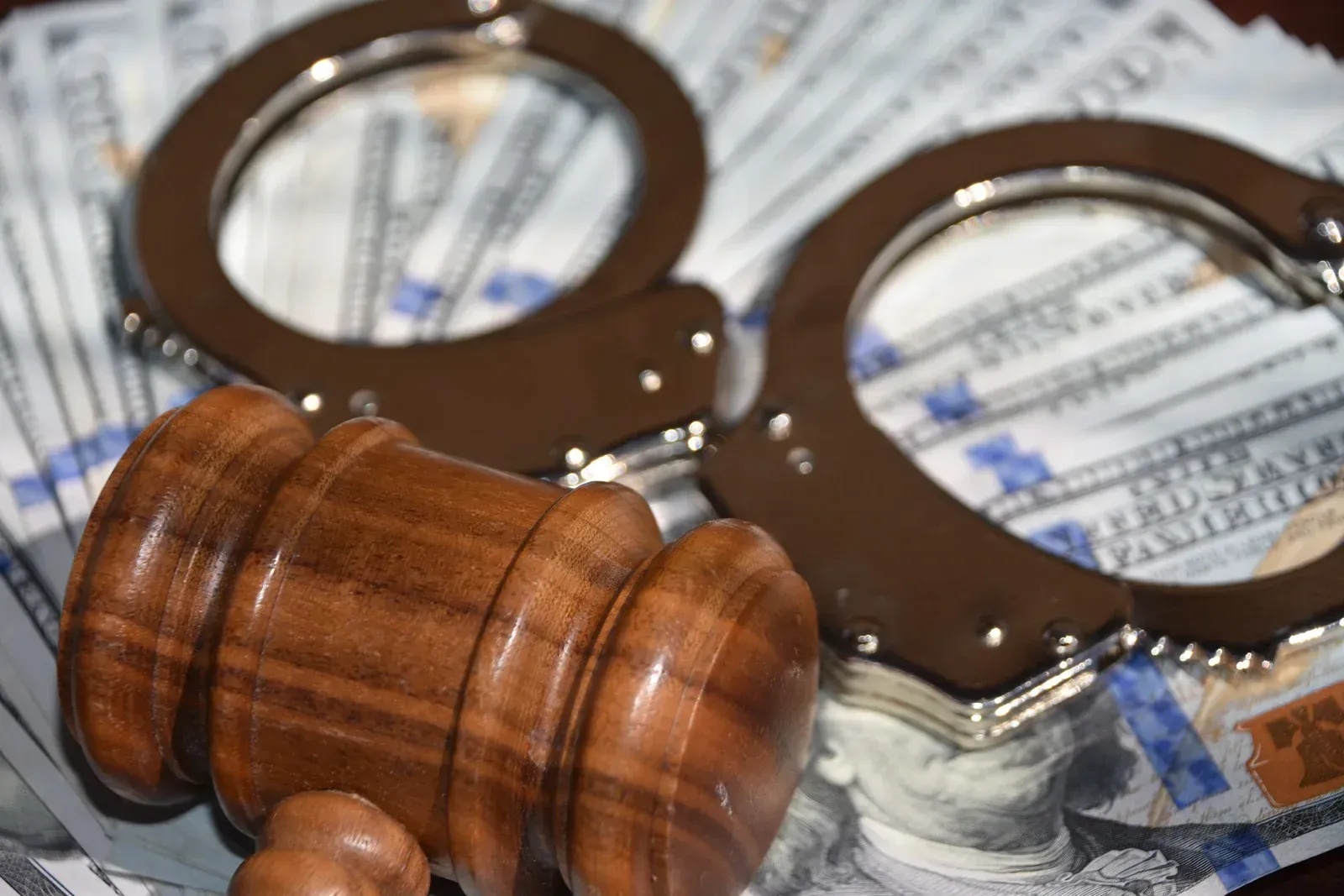 A wooden gavel and handcuffs are sitting on top of a pile of money.