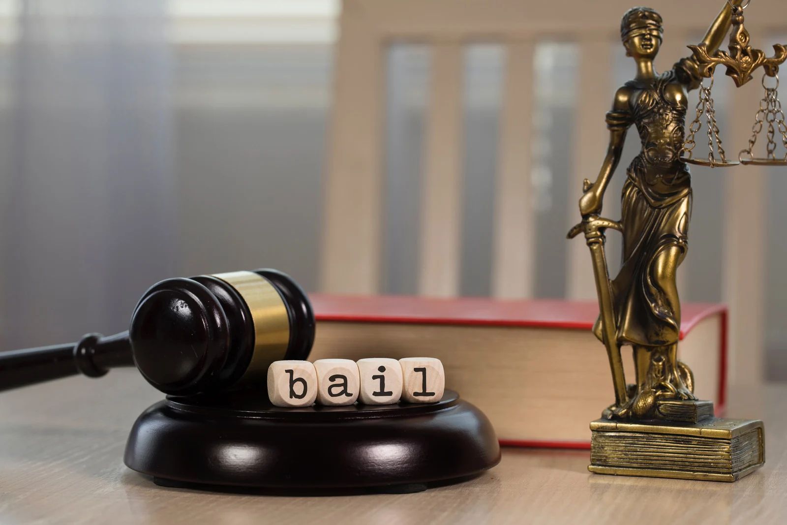 Judge’s gavel and “bail” blocks beside a scales of justice statue on a desk