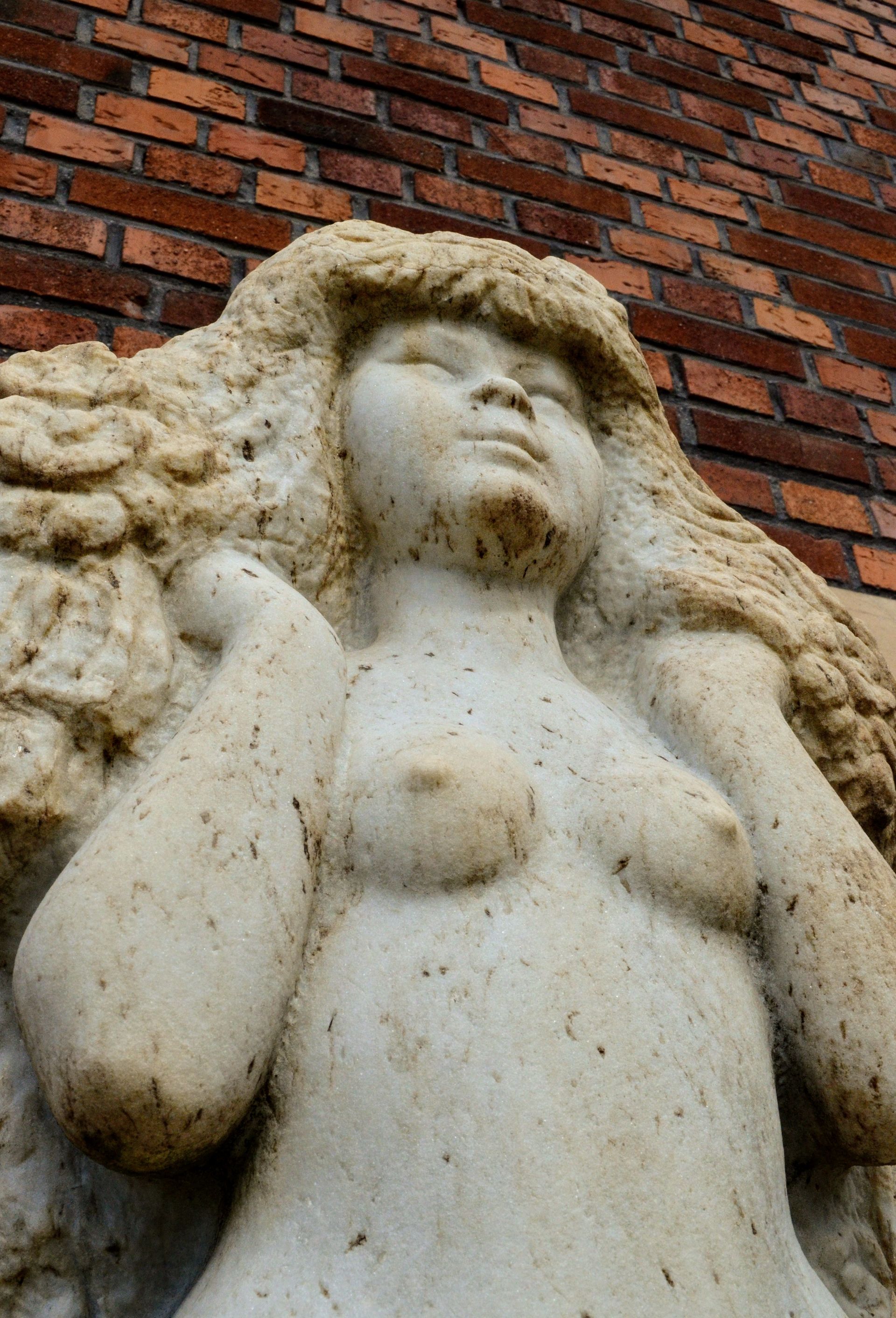En staty av en kvinna med långt hår står mot en tegelvägg.