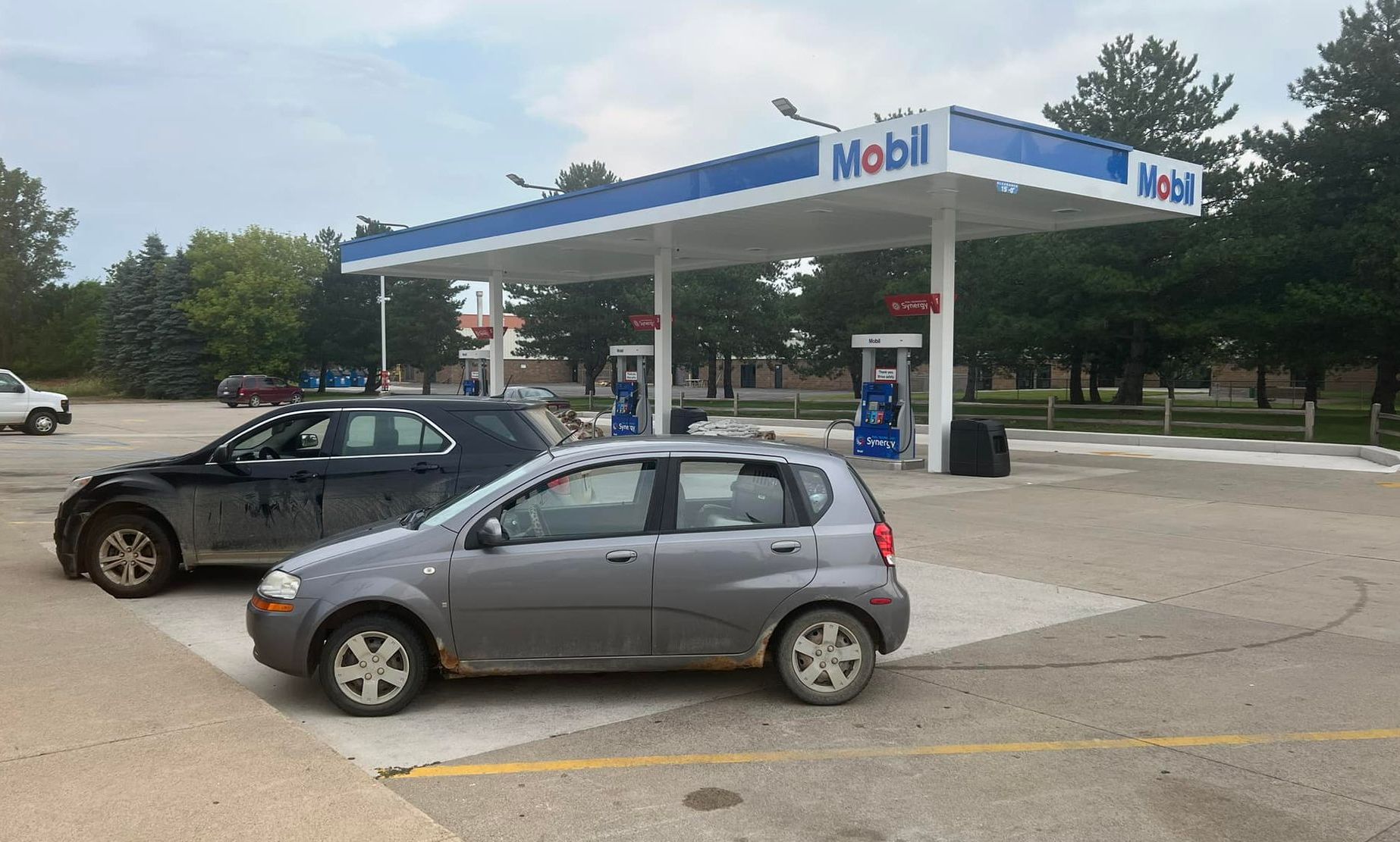 Two cars are parked in front of a mobil gas station.