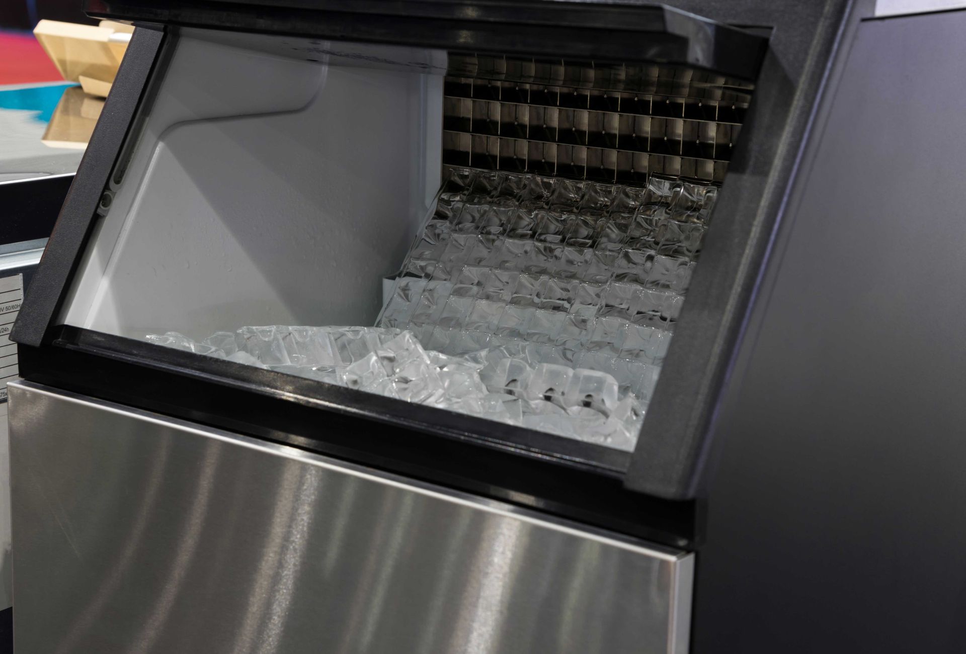 Open commercial ice maker filled with clear square ice cubes inside a stainless steel bin. Open commercial ice maker filled with clear square ice cubes inside a stainless steel bin.