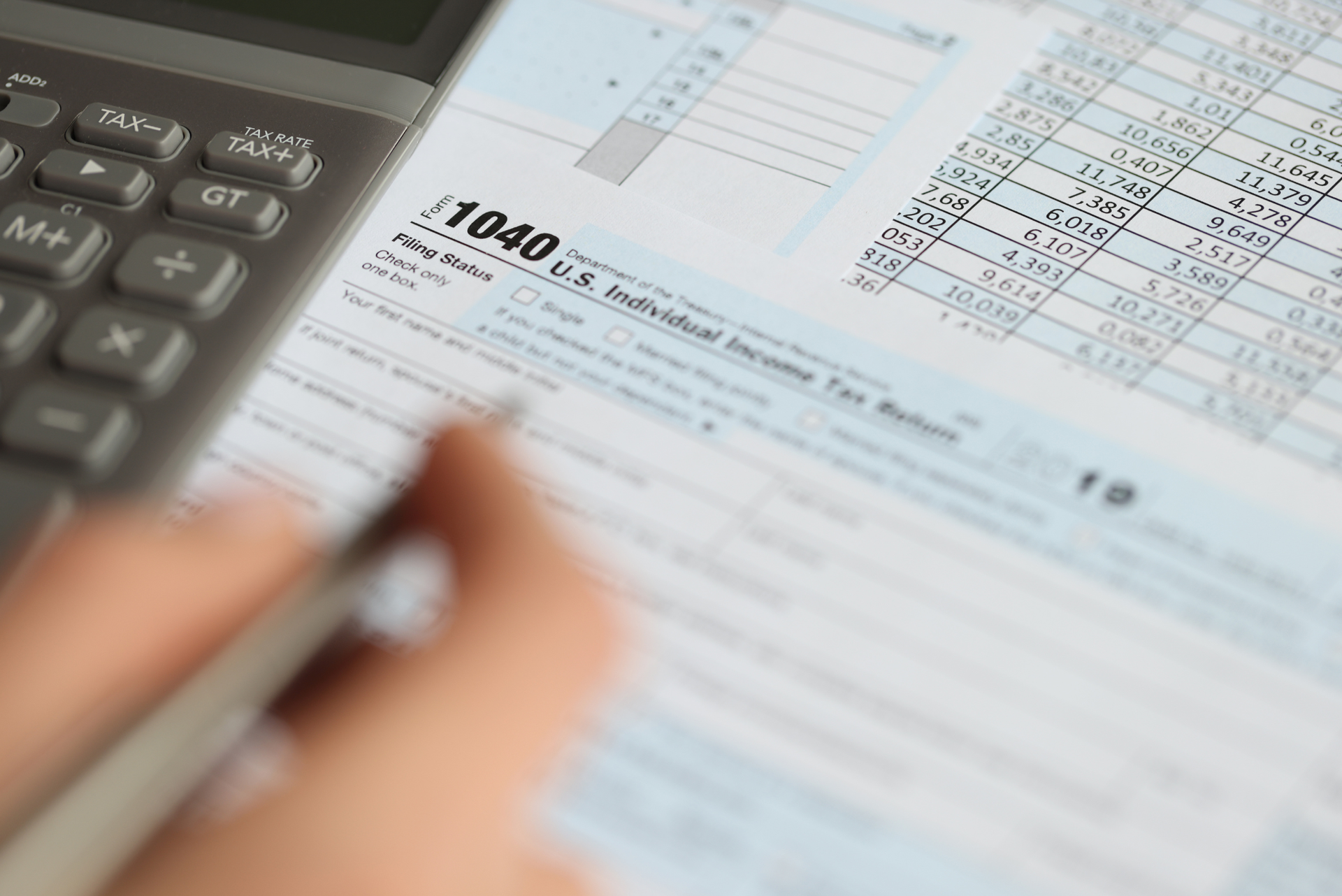 A person is filling out a 1040 tax form with a pen and calculator.