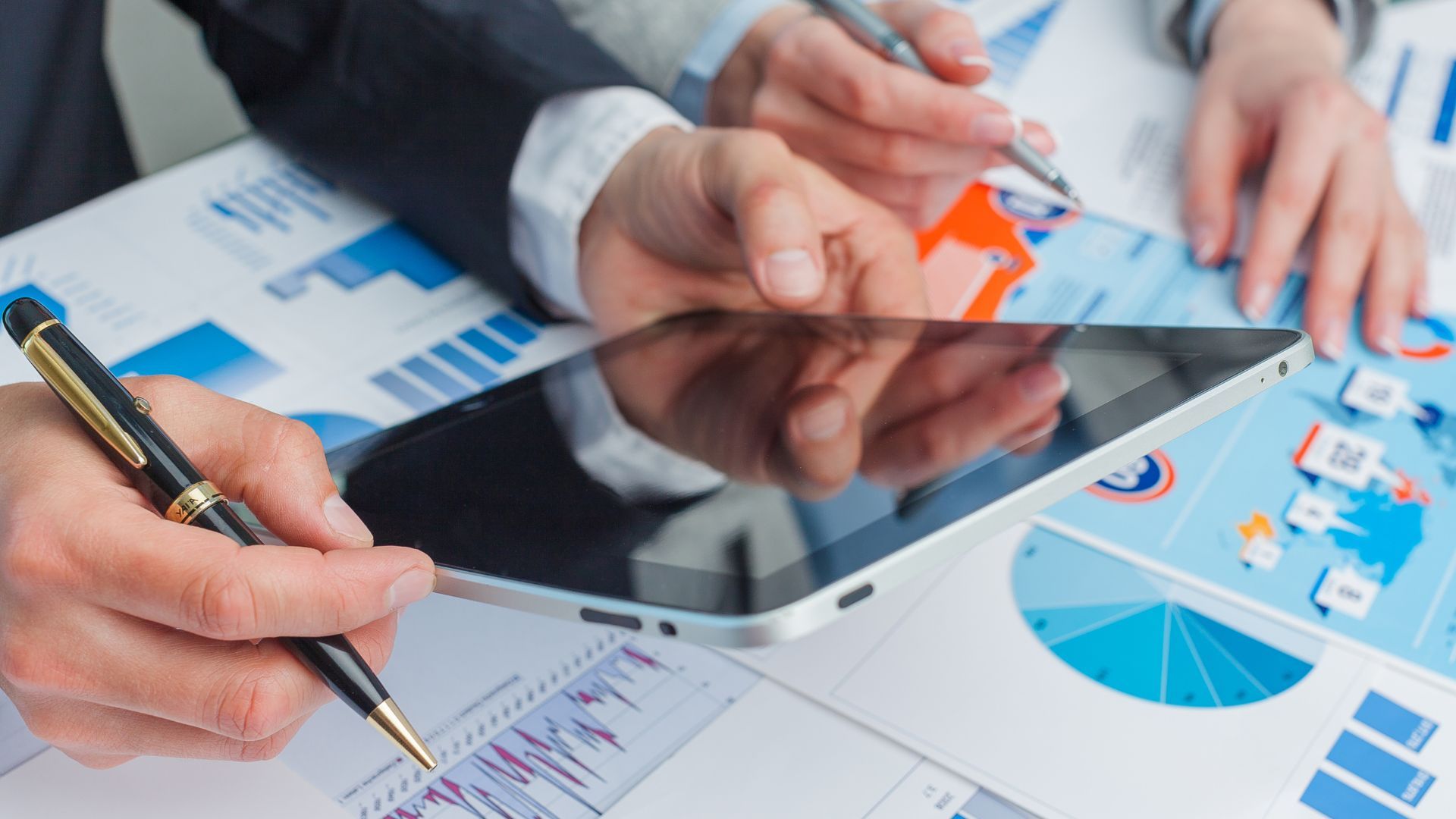 A group of people are sitting at a table looking at a tablet.