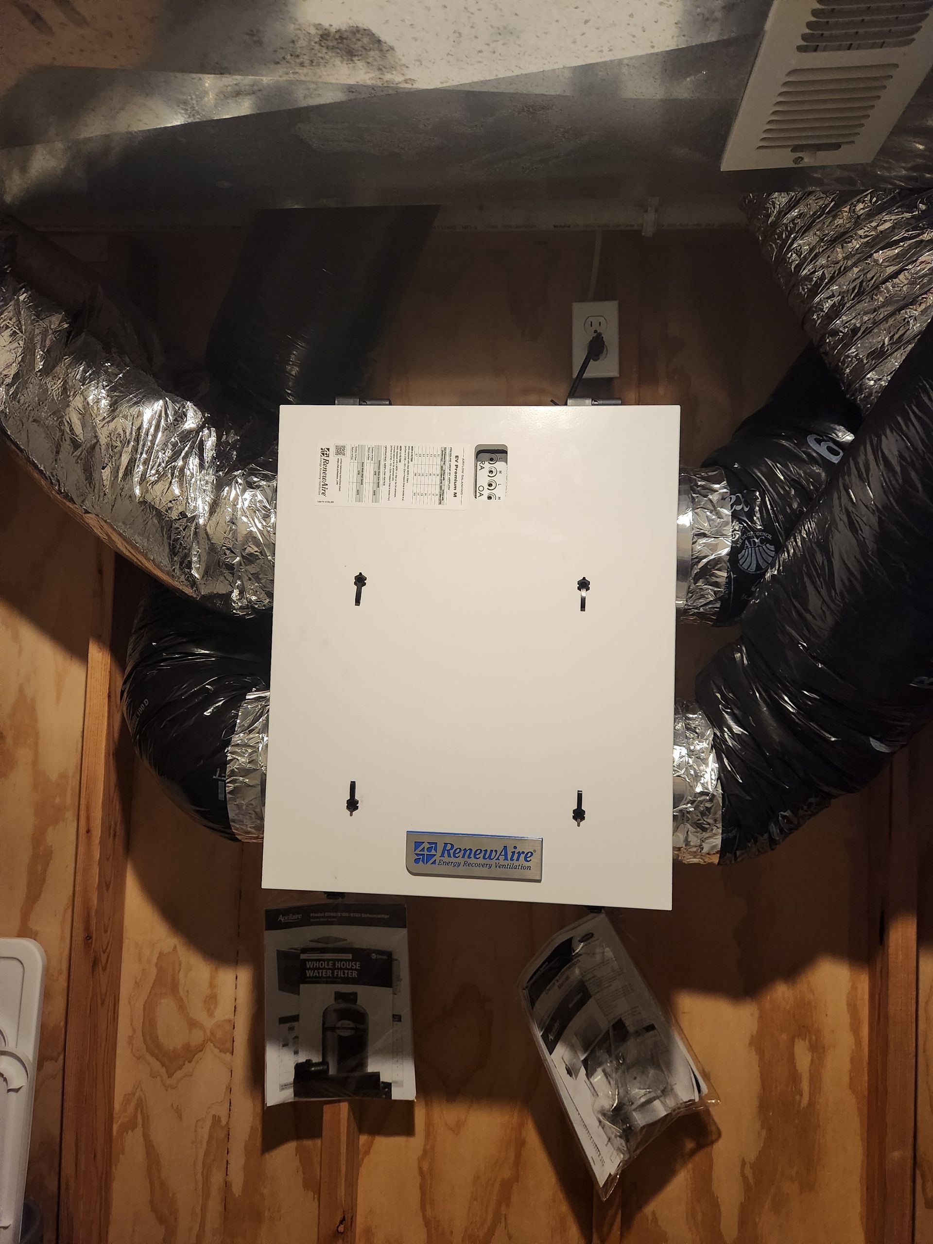 White air purifier with flexible ductwork, mounted on a wood-paneled wall.